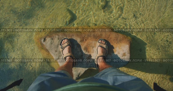 Male feet in sandals stand on river rock by shallow transparent river stream. Стоковое видео, видеограф Ольга Сухарева / Фотобанк Лори