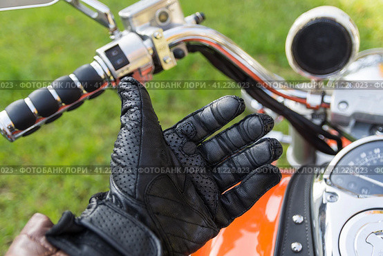 Male hand in the black leather motorcucle glove. Hand in glove is shot against orange motorcycle tank with brown leather riveted tie. Мужская рука в черной кожаной мотоциклетной перчатке. Рука в перчатке запечатлена на фоне оранжевого мотоциклетного бака с коричневым кожаным галстуком с заклепками. Стоковое фото, фотограф Дмитрий Березнев / Фотобанк Лори