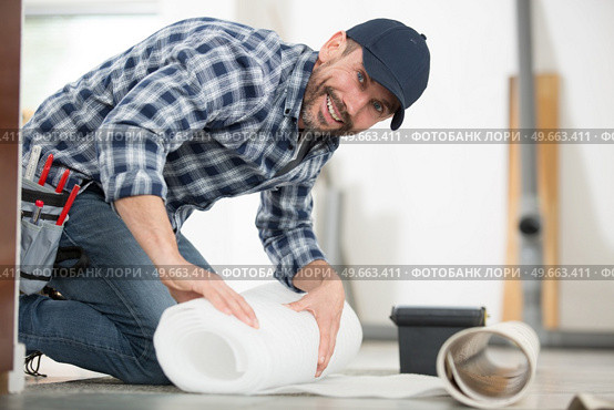 male handyman rolling carpet on floor at home. Стоковое фото, агентство Ingram Publishing / Фотобанк Лори
