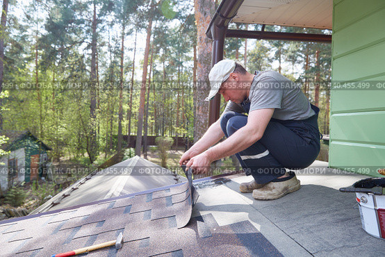 Male worker lays a sheet of soft flexible bitumen shingles on the roof of a country house. Стоковое фото, фотограф Кутина Татьяна / Фотобанк Лори