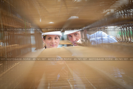 Man and woman looking through stack of metal reinforcing bars. Стоковое фото, агентство Ingram Publishing / Фотобанк Лори
