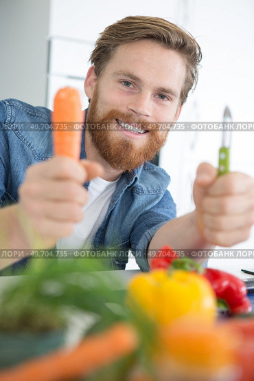 man holding a raw carrot and a peeler. Стоковое фото, агентство Ingram Publishing / Фотобанк Лори