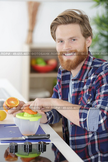 man in kitchen squeezing an orange. Стоковое фото, агентство Ingram Publishing / Фотобанк Лори
