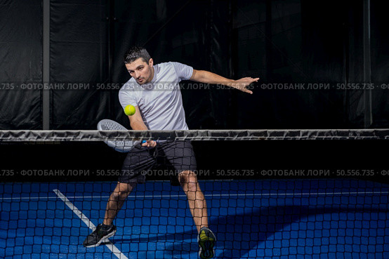 Man playing padel in a blue indoor padel court padel - Young sporty boy padel player hitting ball with a racket. Стоковое фото, агентство Ingram Publishing / Фотобанк Лори