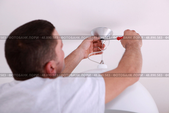 Man repairing ceiling light with screwdriver. Стоковое фото, агентство Ingram Publishing / Фотобанк Лори