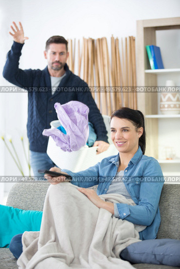 man throwing laundry on lazy wife sitting on sofa. Стоковое фото, агентство Ingram Publishing / Фотобанк Лори