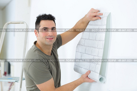 man unrolling roll of brick patterned wallpaper. Стоковое фото, агентство Ingram Publishing / Фотобанк Лори