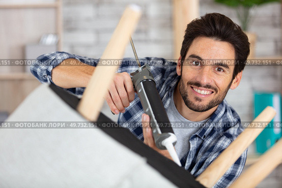 man using sealant gun to repair broken chair. Стоковое фото, агентство Ingram Publishing / Фотобанк Лори