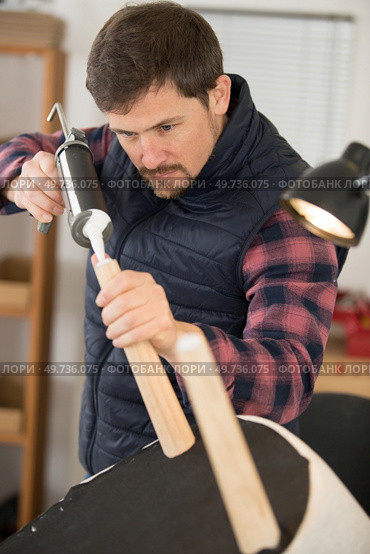 man using sealant gun to repair broken chair. Стоковое фото, агентство Ingram Publishing / Фотобанк Лори