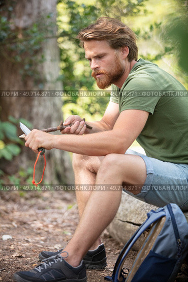 man whittling stick with a blade in the forest. Стоковое фото, агентство Ingram Publishing / Фотобанк Лори