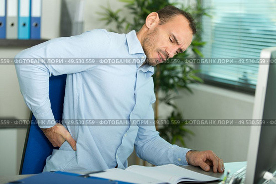 man with back pain in armchair at office. Стоковое фото, агентство Ingram Publishing / Фотобанк Лори