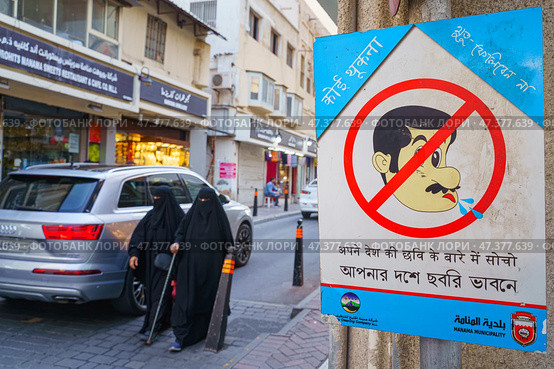 Manama, Bahrain - Jan 08 2024, A view of the street with pedestrians, half of the frame is occupied by a warning sign prohibiting spitting, Manama, Bahrain. Редакционное фото, фотограф Сергей Богомяко / Фотобанк Лори