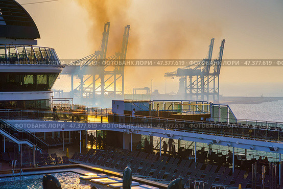 Manama, Bahrain - Jan 08 2024, Panoramic view of Bahrain commercial port with blue cranes, with upper deck of MSC Virtuosa cruise ship on foreground, by the morning, dawn, sunrise, Manama, Bahrain. Редакционное фото, фотограф Сергей Богомяко / Фотобанк Лори