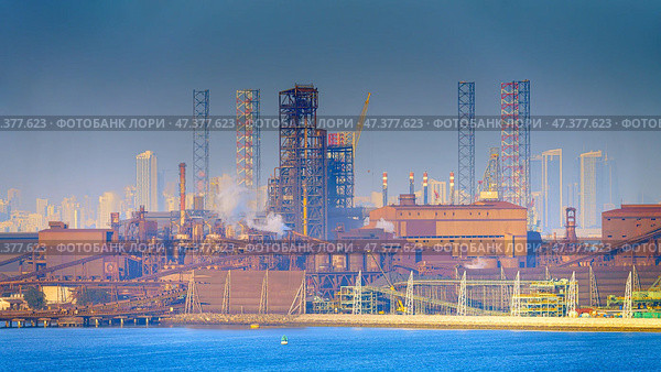 Manama, Bahrain- Jan 08 2024, Panoramic view of the industrial port buildings, constructions, the skyscrapers of Manama are visible in the distance, in the daytime, Manama, Bahrain. Редакционное фото, фотограф Сергей Богомяко / Фотобанк Лори