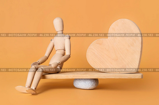 Mannequin and wooden heart on teeterboard against color background. Concept of balance. Стоковое фото, фотограф Pixel_shot / Фотобанк Лори