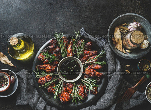 Marinated fried chicken wings with sauce and rosemary on dark plate at rustic black table with oil, spices and tablecloth. Top view with copy space. Стоковое фото, агентство Ingram Publishing / Фотобанк Лори