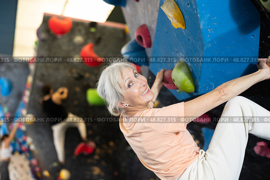 Mature female fitness climber training at bouldering gym.Woman rise up on artificial climbing wall. Стоковое фото, фотограф Яков Филимонов / Фотобанк Лори