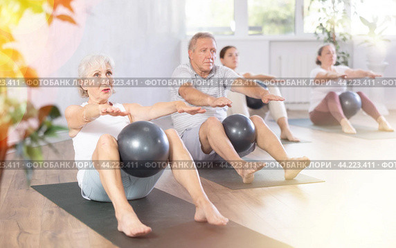 Mature people with young coach sit on karemat, pulled leg to themselves and clamped softball in knee. Стоковое фото, фотограф Яков Филимонов / Фотобанк Лори