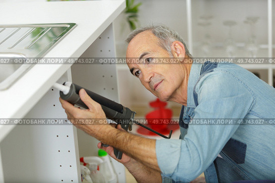 mature plumber fills the seam between the sink and furniture. Стоковое фото, агентство Ingram Publishing / Фотобанк Лори