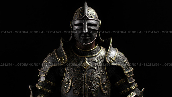 Medieval knight wearing ornate armor and helmet posing against black background. Стоковое фото, фотограф David Kashakhi / Фотобанк Лори