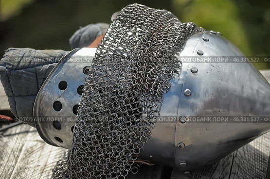 Medieval knightly equipment, including a conical helmet with rivets, a chainmail aventail and a balaclava made of thick fabric. The helmet is made of metal, polished and has ventilation holes. The chainmail aventail is designed to protect the neck and shoulders from weapon blows.This element of armor is typical for medieval Europe and was widely used by knights and warriors in battle. Perhaps this is part of the ammunition used in historical reconstructions or museum exhibitions. Стоковое фото, фотограф Анна Кривицкая / Фотобанк Лори