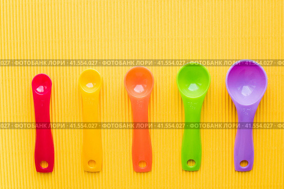 Мерные ложки на желтом фоне. Разноцветные пластиковые мерные ложки. Measuring spoons on a yellow background. Multi-colored plastic measuring spoons. Стоковое фото, фотограф Ольга Митряева / Фотобанк Лори