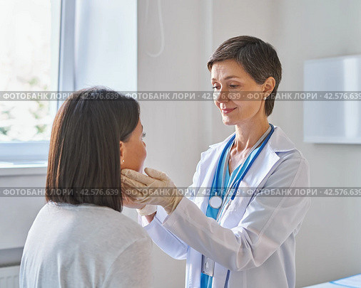 Middle-aged woman doctor wearing gloves checking patients sore throat or thyroid glands. Стоковое фото, фотограф Natalia Gdovskaia / Фотобанк Лори