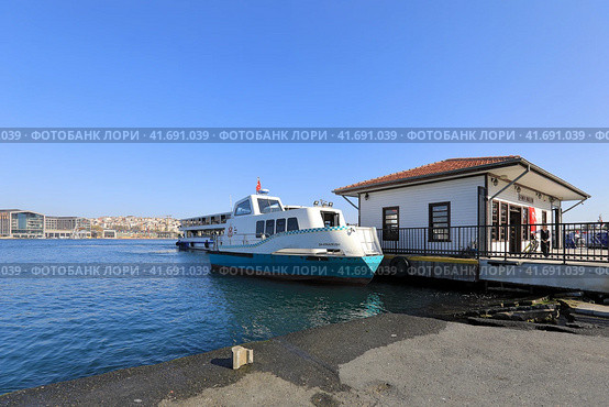 Modern building of the Fener ferry pier on the shore of the Golden Horn. Vessel standing on the pier. District of Fatih, city of Istanbul, Turkey. (2023 год). Редакционное фото, фотограф Bala-Kate / Фотобанк Лори