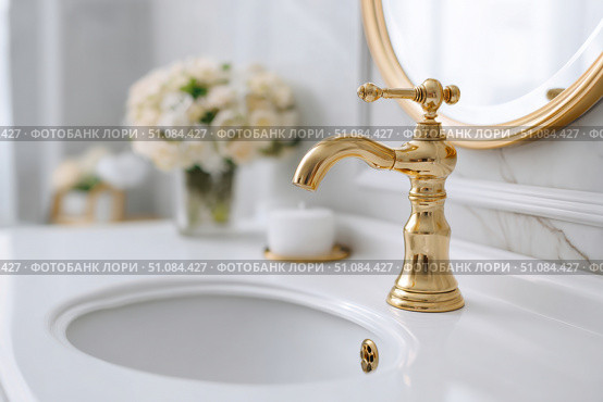 Modern golden faucet and marble stone sink. Stylish white sink, faucets in a light interior. Copper brass tap. Domestic Appliances. Clean bright bathroom. Household equipment. New Contemporary style. Стоковое AI-изображение, AI-художник Марина Демидюк / Фотобанк Лори