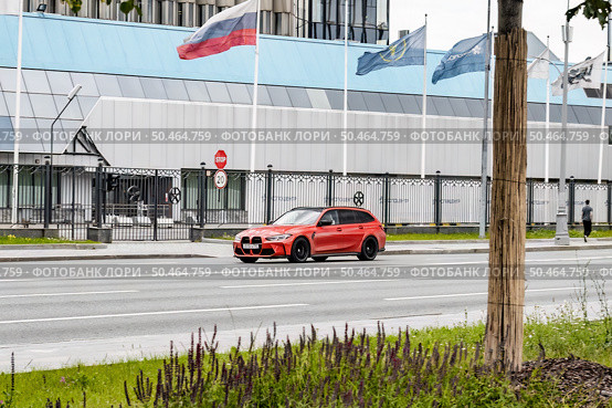 Modern red estate car BMW M3 Competition Touring driving fast on highway with blurred motion and city buildings in background. Редакционное фото, фотограф Константин Григорьев / Фотобанк Лори