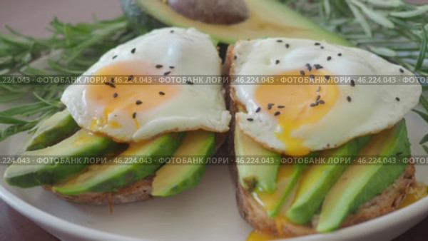 Modern Two Toasts with avocado and fried egg Spreading Yolk, rosemary 4K. Preparing healthy toast breakfast avocado slices rye wholegrain bread, sunny side up egg on top. breakfast for two, couple. Стоковое видео, видеограф Елизавета Малкова / Фотобанк Лори