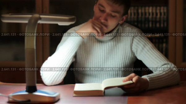 Молодой человек читает книгу за рабочим столом. Снято слайдером. Стоковое видео, видеограф ILLYCH / Фотобанк Лори