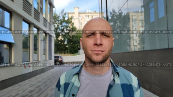 Молодой человек медленно идет по переулку между двумя офисными зданиями. Симпатичный парень в клетчатой рубашке. Красивый мужчина гуляет по городской улице теплым солнечным днем. Крупный план, вид спереди. Young man walks down an alley between two office buildings. Cute bald guy in a plaid shirt. White caucasian man walks slowly along city street on a warm sunny day. Close-up, front view. Стоковое видео, видеограф Ирина / Фотобанк Лори