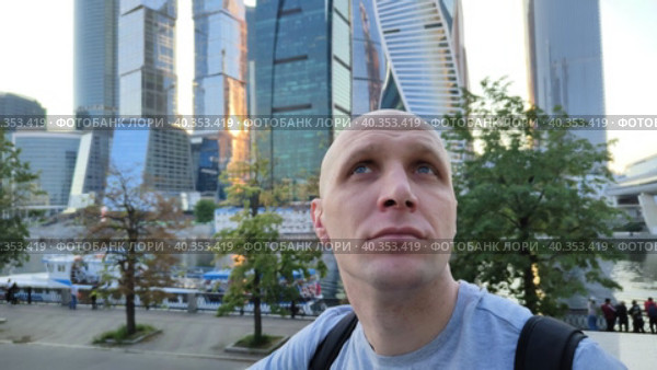 Молодой человек восхищается архитектурой современного города. Парень смотрит по сторонам. Мужчина путешествует по городам мира и России. Стеклянные здания и набережная реки. Вид на Москва Сити. A young man admires the architecture of a modern city. The guy looks around. A man travels around the cities of the world and Russia. Glass buildings and the river embankment. View of Moscow City. Стоковое видео, видеограф Ирина / Фотобанк Лори