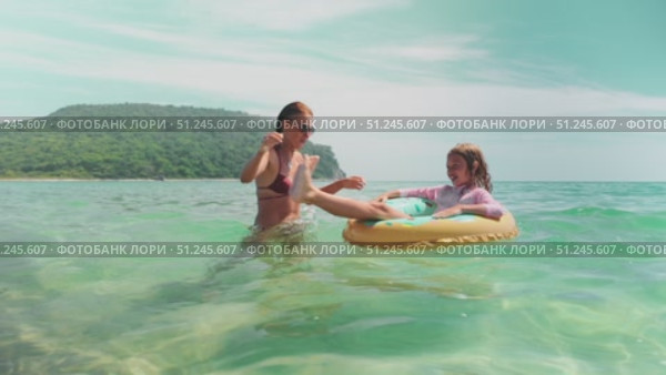 Mom and daughter laugh together as girl floats in donut ring. Pure beach joy, captured in turquoise water under sunny sky. Ideal image of summer vacation and loving family moment. Стоковое видео, видеограф Енваев Андрей / Фотобанк Лори
