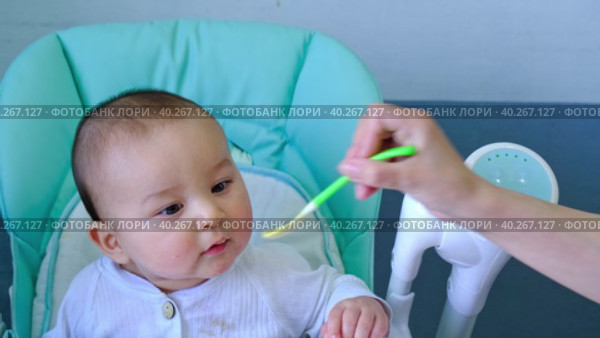 Mom feeds the baby with a spoon of vegetable puree at the children's feeding table. Baby's appetite, healthy nutrition, introduction of complementary foods. Copyspace, mock up. Стоковое видео, видеограф Ольга Симонова / Фотобанк Лори