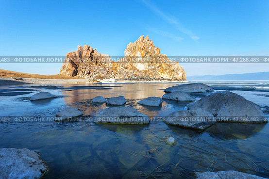 Morning on Lake Baikal during spring ice drift. View of famous Shamanka Rock - natural landmark of Olkhon Island. Bay is covered with thin transparent crust of blue ice. Scenic landscape. Change seasons. Стоковое фото, фотограф Виктория Катьянова / Фотобанк Лори
