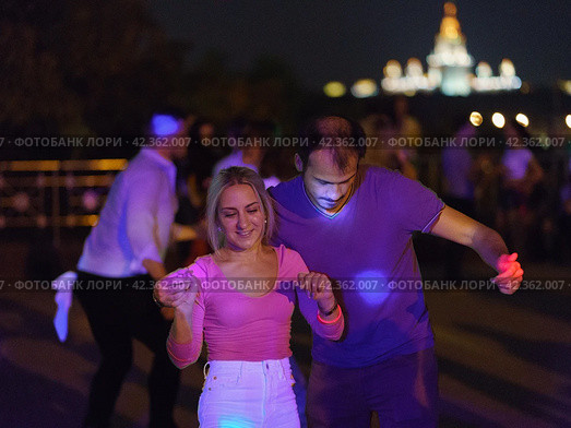 Moscow, Russia - August 20, 2019: Defocused photography of beautiful dancing people on the night party in the city street in  summer night.  Leisure, happiness and entertainment theme. Редакционное фото, фотограф YuryKara / Фотобанк Лори