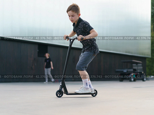 Moscow, Russia - July 26, 2019 Teenager ready to perform a trick at sportive push scooter on a city street. Редакционное фото, фотограф YuryKara / Фотобанк Лори