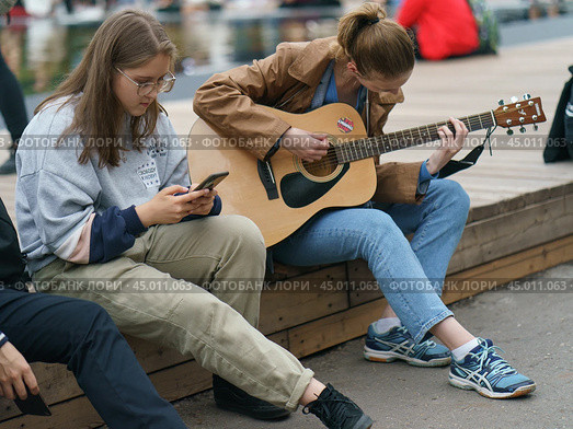 Moscow, Russia - September 5, 2019: Portraits of young women visiting the city festival in the Gorky park. Somebody play guitar, somebody play smartphone. Blurred background. Редакционное фото, фотограф YuryKara / Фотобанк Лори