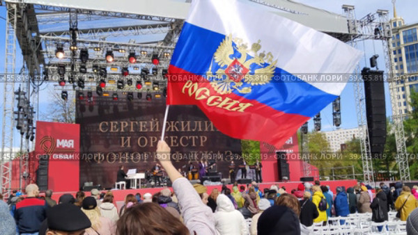 МОСКВА, РОССИЯ - 9 мая 2022 года: Люди в парке Музеон смотрят концерт, посвященный великому празднику - Дню Победы. Женщина размахивает российским флагом. Выступление Сергея Жилина и оркестра "Фонограф Джаз". MOSCOW, RUSSIA - MAY 9, 2022: People in Muzeon Park watch a concert dedicated to the great holiday - Victory Day. A woman waves a Russian flag. Performance by Sergey Zhilin and the Phonograph Jazz Orchestra. Редакционное видео, видеограф Ирина / Фотобанк Лори