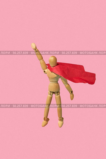 Movable miniature articulation mannequin in a red cape is flying up with raised hand as a superhero or superman against pink background, copy space. Business success and leadeship concept.. Wooden mannequin miniature doll in a red cape flies up as a superman. Стоковое фото, агентство Ingram Publishing / Фотобанк Лори