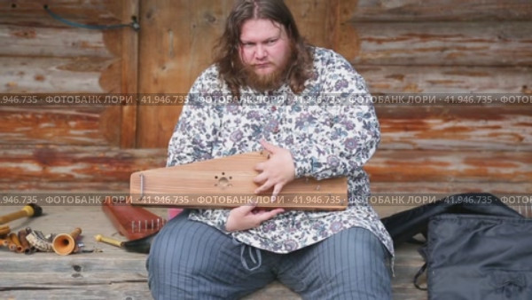Musician in russian clothing teaches to playing on ancient musical instrument gusli (harp) (2022 год). Редакционное видео, видеограф FotograFF / Фотобанк Лори
