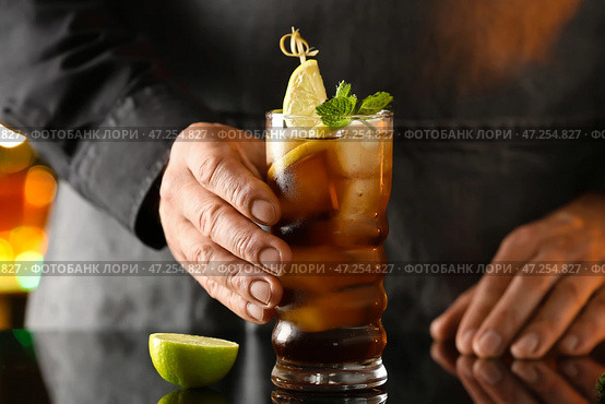 Мужчина-бармен со стаканом вкусного коктейля Cuba Libre на столе в баре. Стоковое фото, фотограф Pixel_shot / Фотобанк Лори