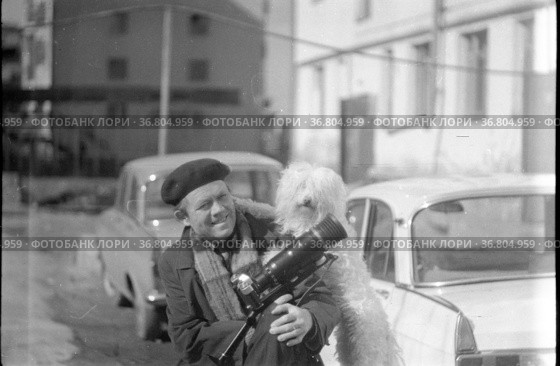Мужчина фото-журналист, портрет фотографа во дворе домов, он улыбается и позирует рядом с собакой, человека с фотоаппаратом рядом с домами и машинами , Тетерин, Фатпулов, Долли, Якутия, май 1980 года. Редакционное фото, фотограф Варфоломей Тетерин / Фотобанк Лори