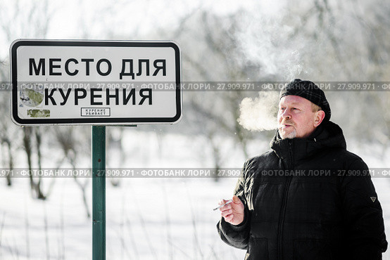 Мужчина курит сигарету возле таблички "Место для курения" Стоковое фото, фотограф Игорь Низов / Фотобанк Лори