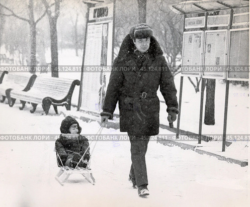 Мужчина в ушанке везёт ребёнка на санках. 1970-1980 гг СССР. Стоковое фото, фотограф Retro / Фотобанк Лори