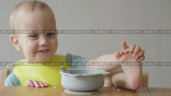 Naughty baby child putting foot leg on table while eating having lunch in kitchen. Стоковое видео, видеограф Olesia Kondrateva / Фотобанк Лори
