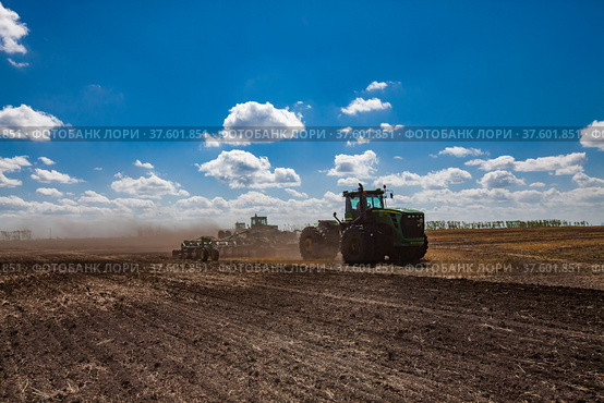 North Kazakhstan Province, Kazakhstan - May 12, 2012: Sowing campaign. John Deere tractors cultivating soil with harrow. Blue sky, clouds. Редакционное фото, фотограф Alexey Rezvykh / Фотобанк Лори