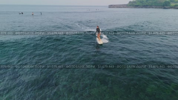 November 26, 2024. Bali, Indonesia. Surfer woman rides on surfboard in blue ocean with crashing ocean wave. Редакционное видео, видеограф Wonderful nature / Фотобанк Лори